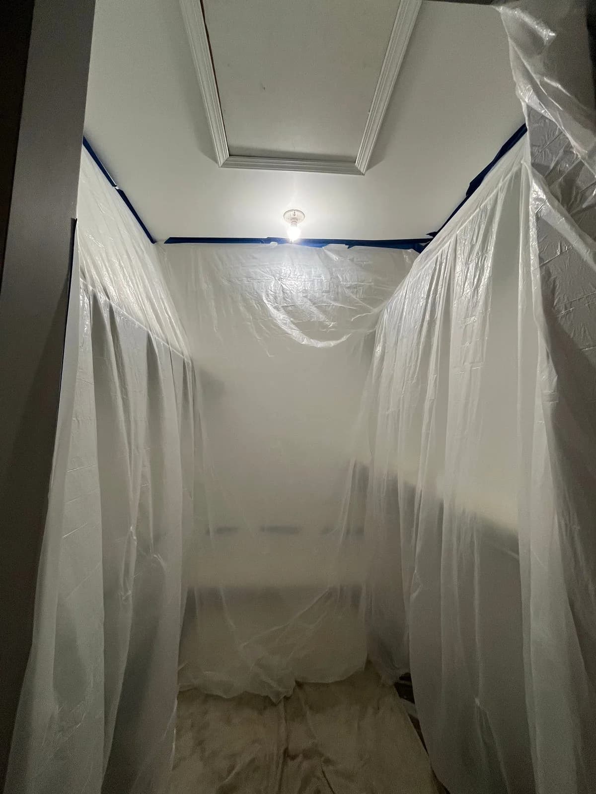 Plastic sheeting taped from the ceiling to the floor around an attic access opening