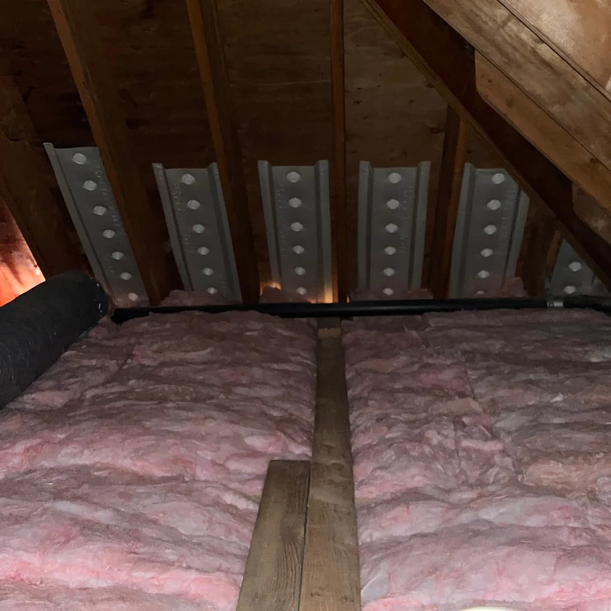 Pink fiberglass batts between attic joists with baffles installed along the eaves